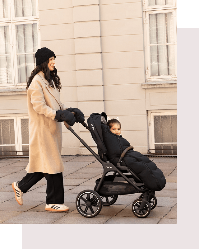 A warmly dressed woman pushes her child in the TRIVlx puschair with the TRIV lx all-in-one set accessories. 