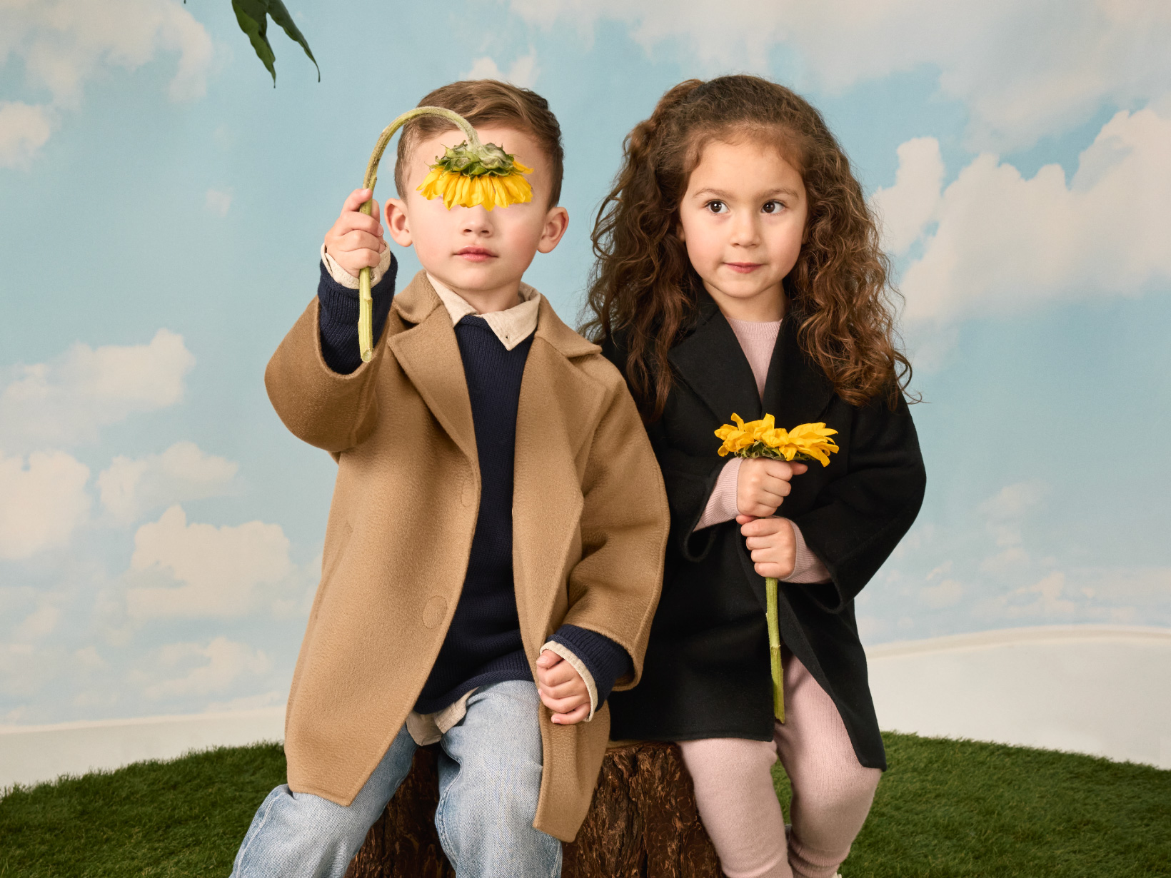 A girl and boy holding sunflowers wearing matching Nuna Cashmere Coats, in Camel and Shadow fashion