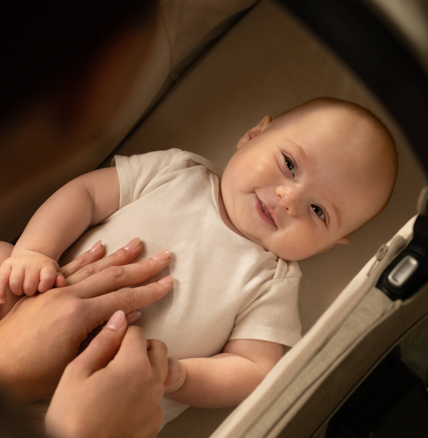 Un bambino sorridente sdraiato nella navicella del passeggino Nuna MIXX next nel colore Chateau.
