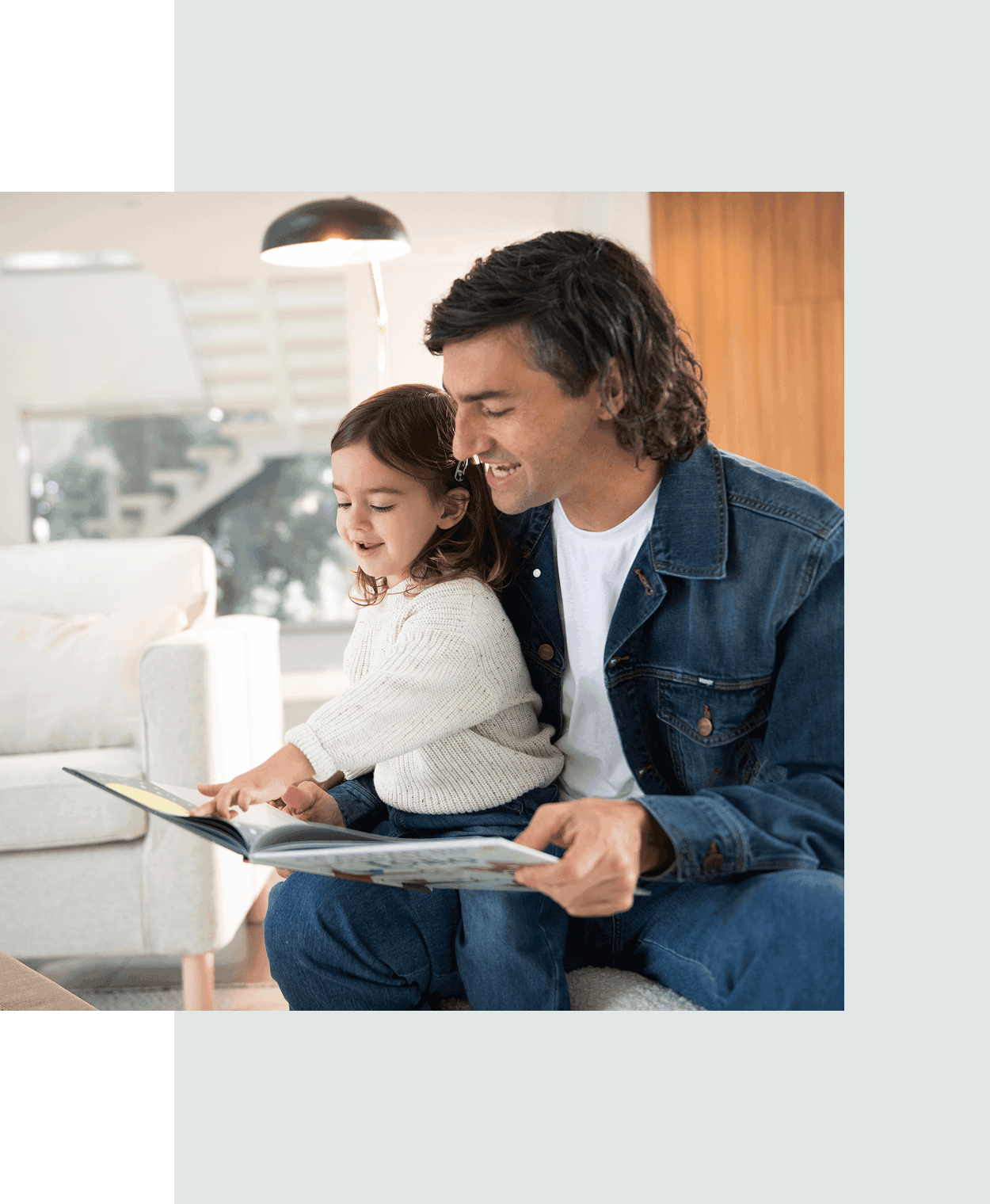 Un padre y su hija leen juntos un libro en el sof&aacute;.