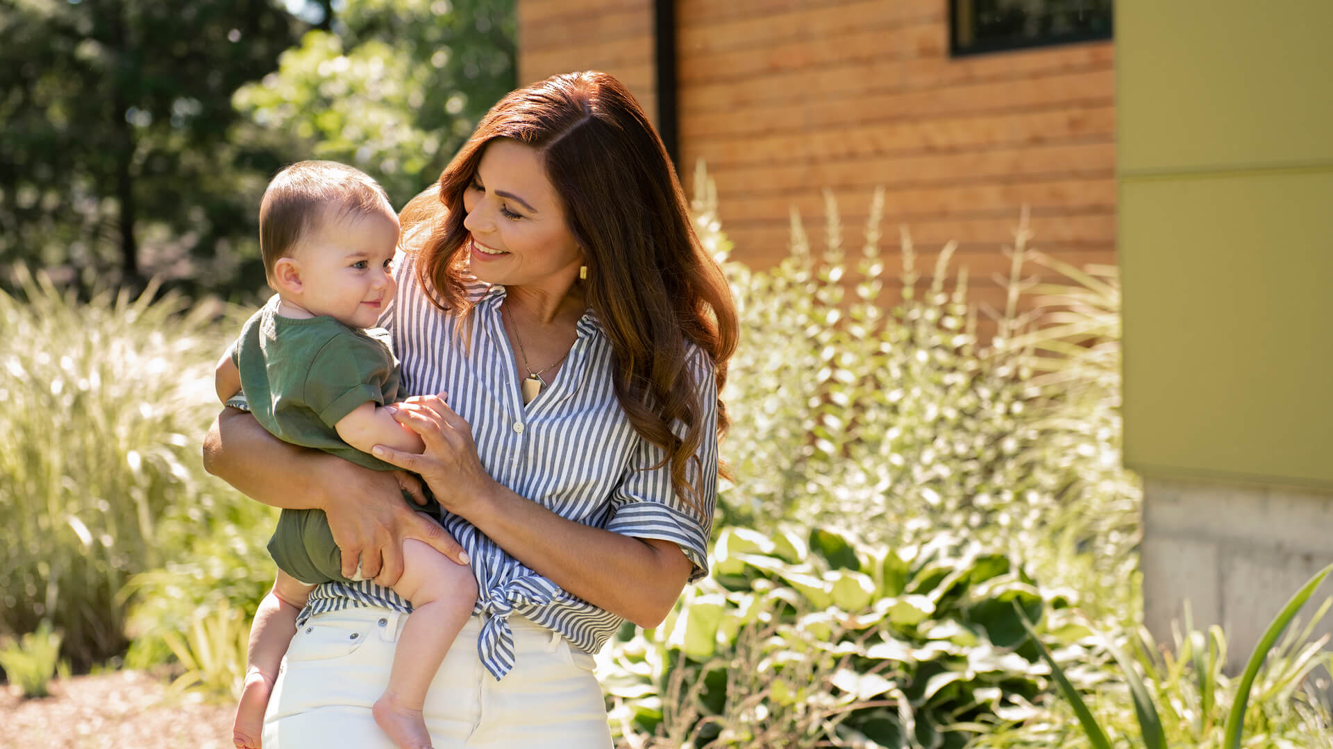 A mother holds her young child outside on a sunny day.