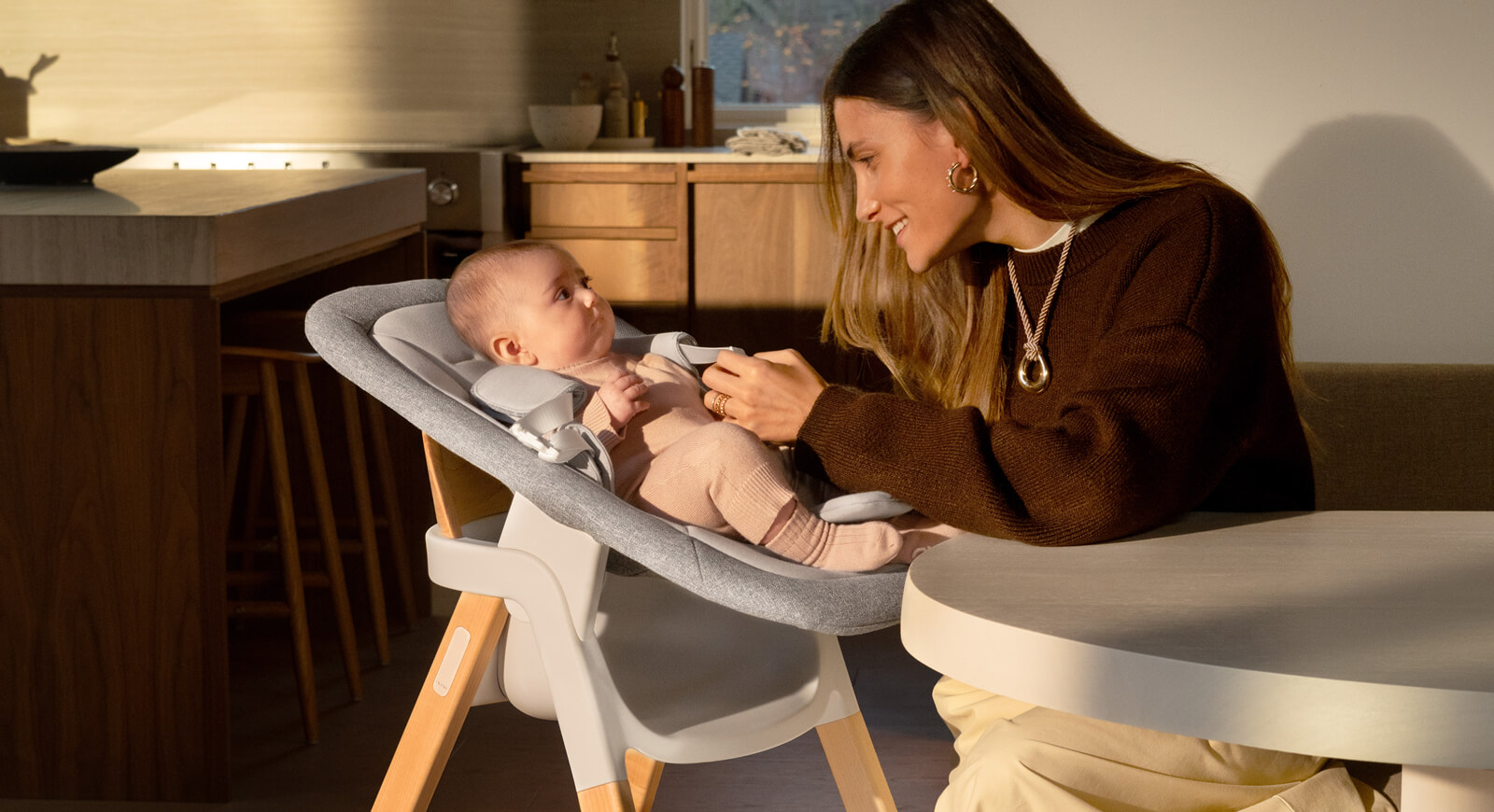 A mother smiles at her infant while they recline in the newborn rocker attachment on the BRYN highchair.
