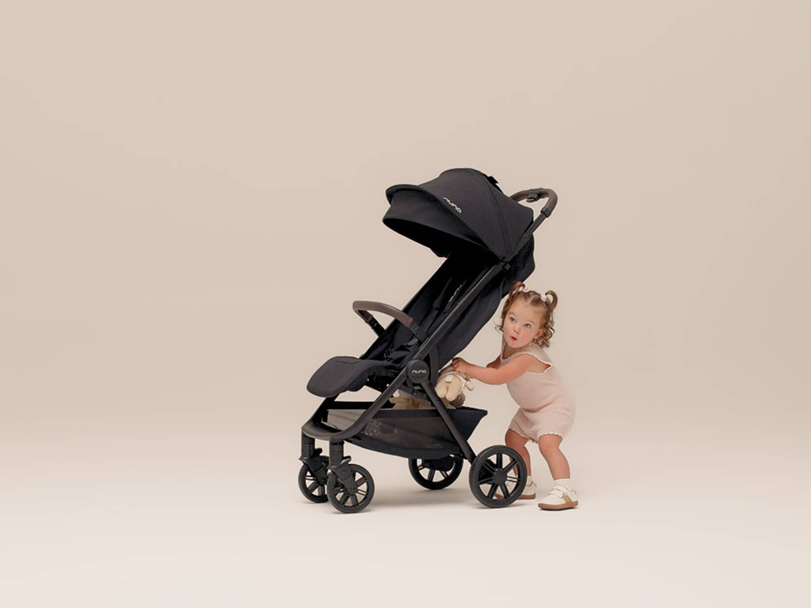 A toddler pulls her stuffed animal from the basket of the TRVL urbn pushchair.