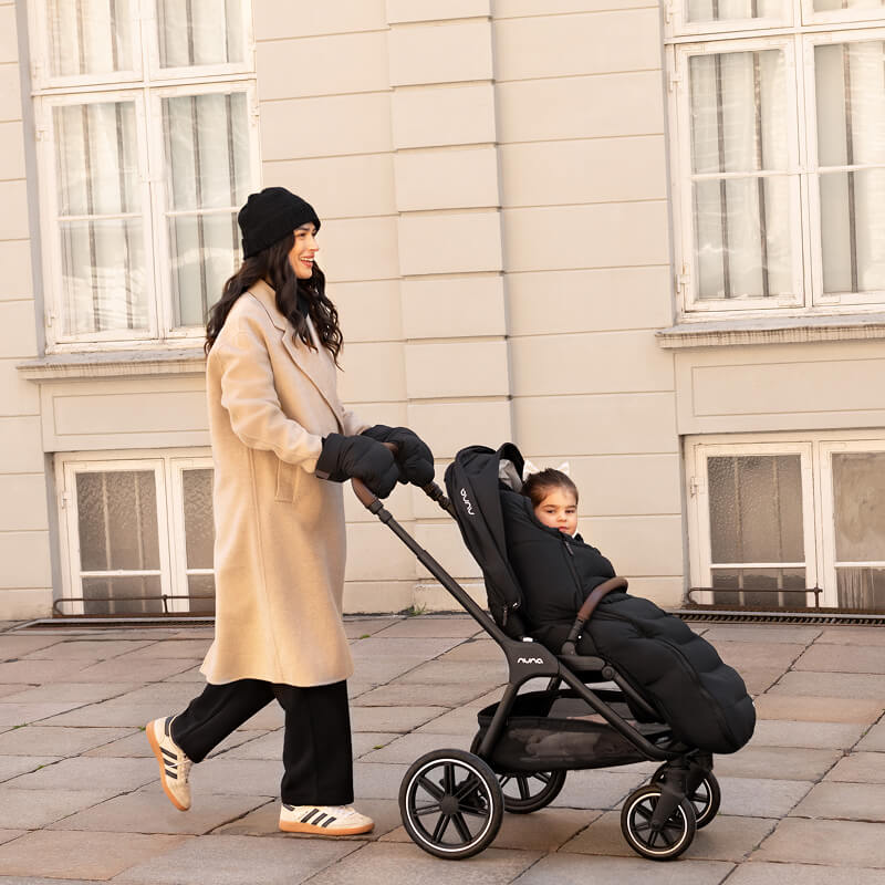 A warmly dressed woman pushes her child in the TRIVlx puschair with the TRIV lx all-in-one set accessories. 