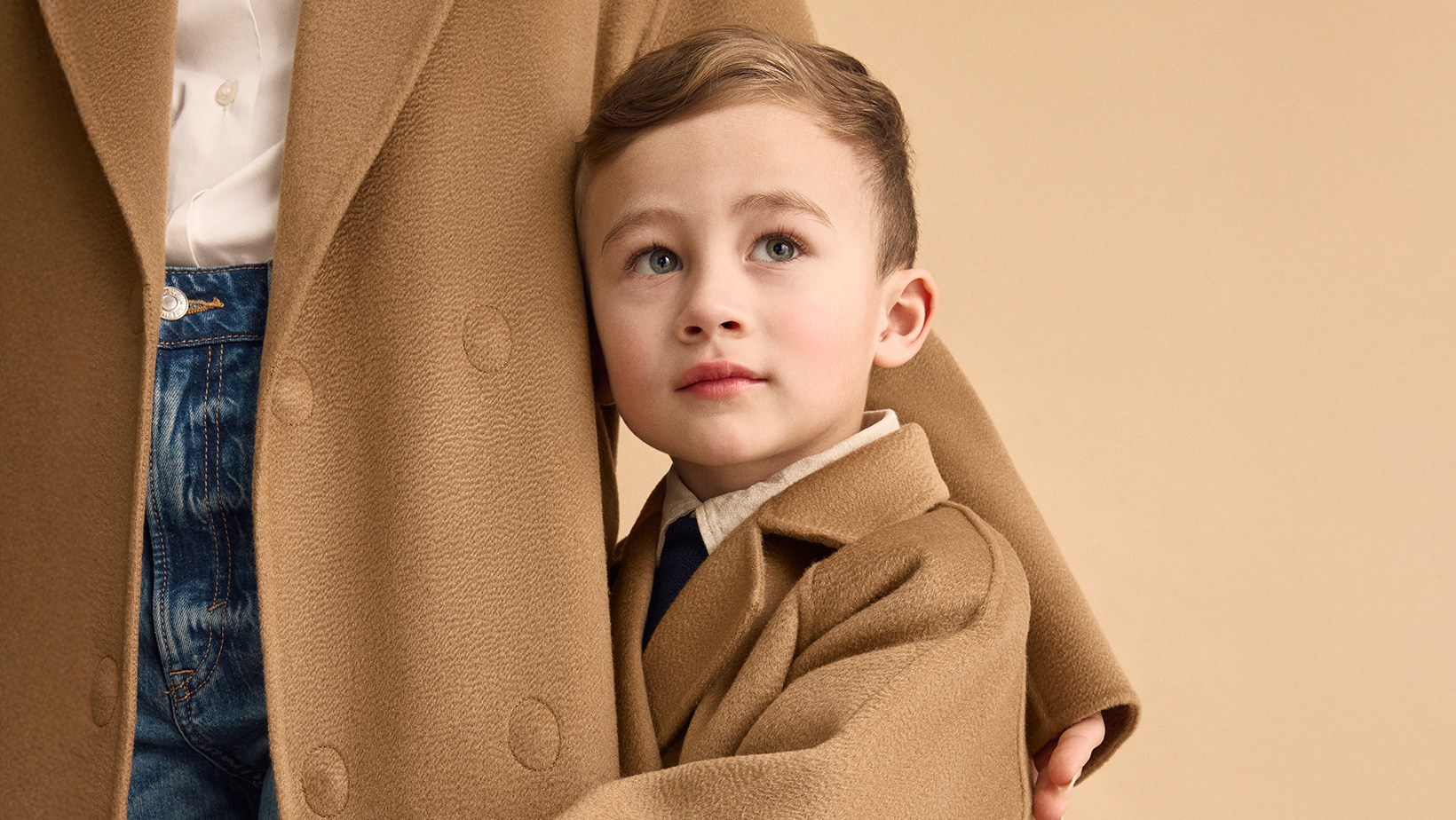 A close up of a young boy standing in front of a woman wearing a Nuna Cashmere Coat in Camel fashion