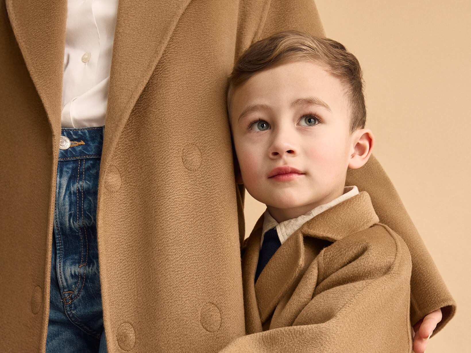 A close up of a young boy standing in front of a woman wearing a Nuna Cashmere Coat in Camel fashion