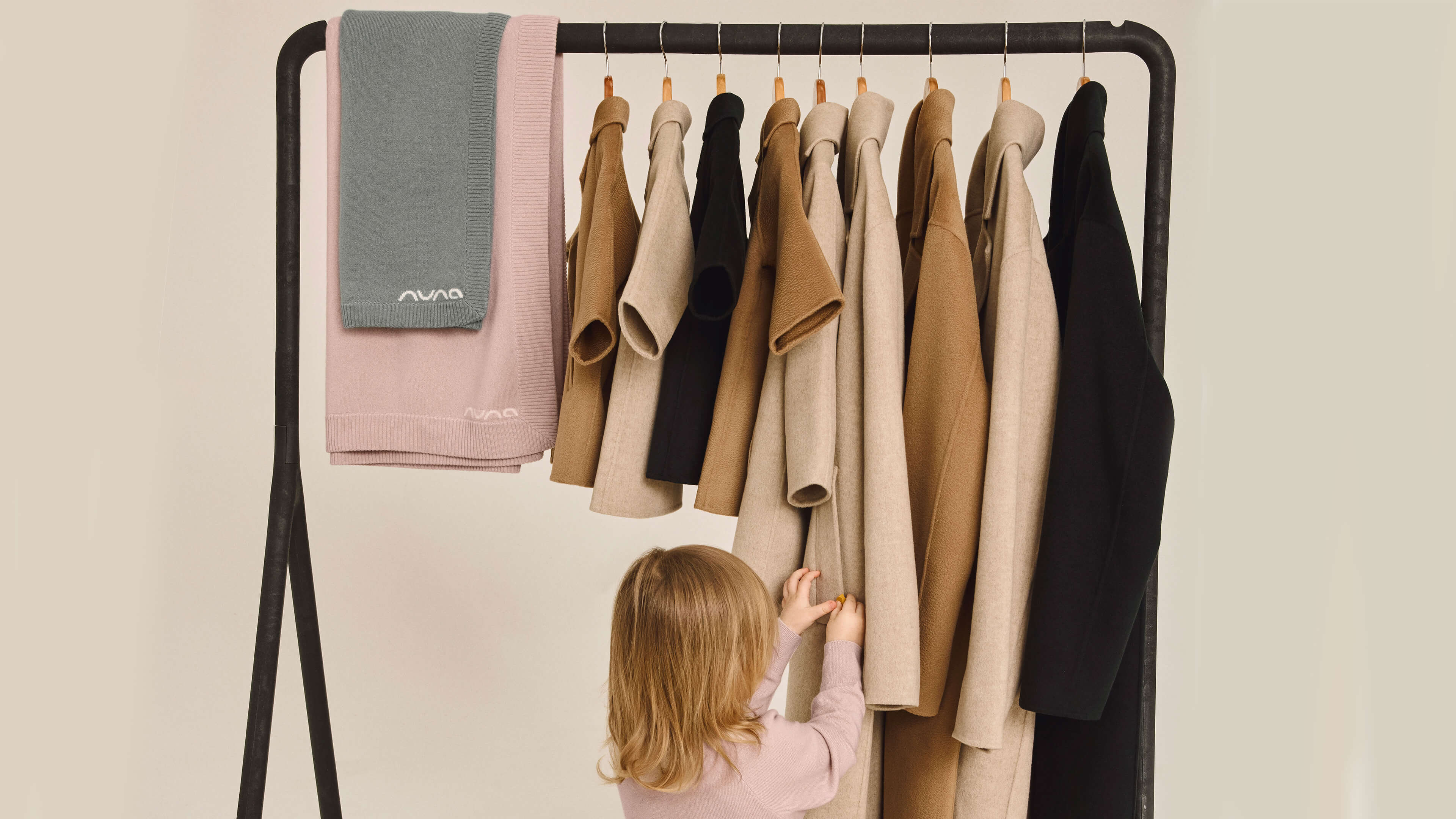 A young girl facing away looking at a clothes rail wearing the Nuna Cashmere Two-Piece Sweater Set and Socks in Dusty Mauve
