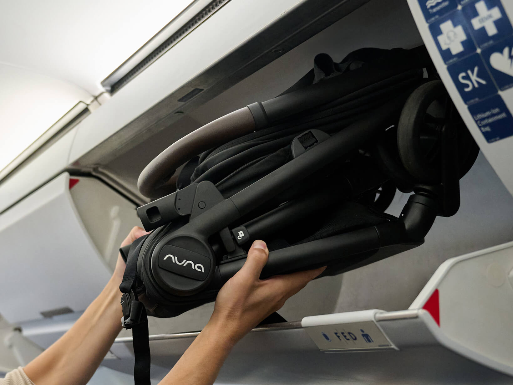 A man easily loads a folded VIAA cabn pushchair into an airplane overhead bin.