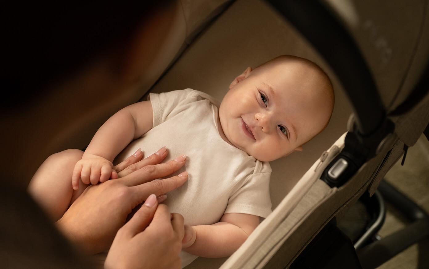 An infant smiles while laying on the MIXX next carry cot mattress.