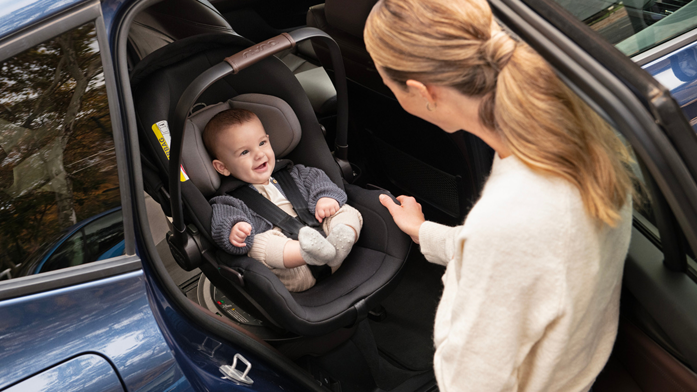 Smiling baby buckled into a Nuna infant car seat.