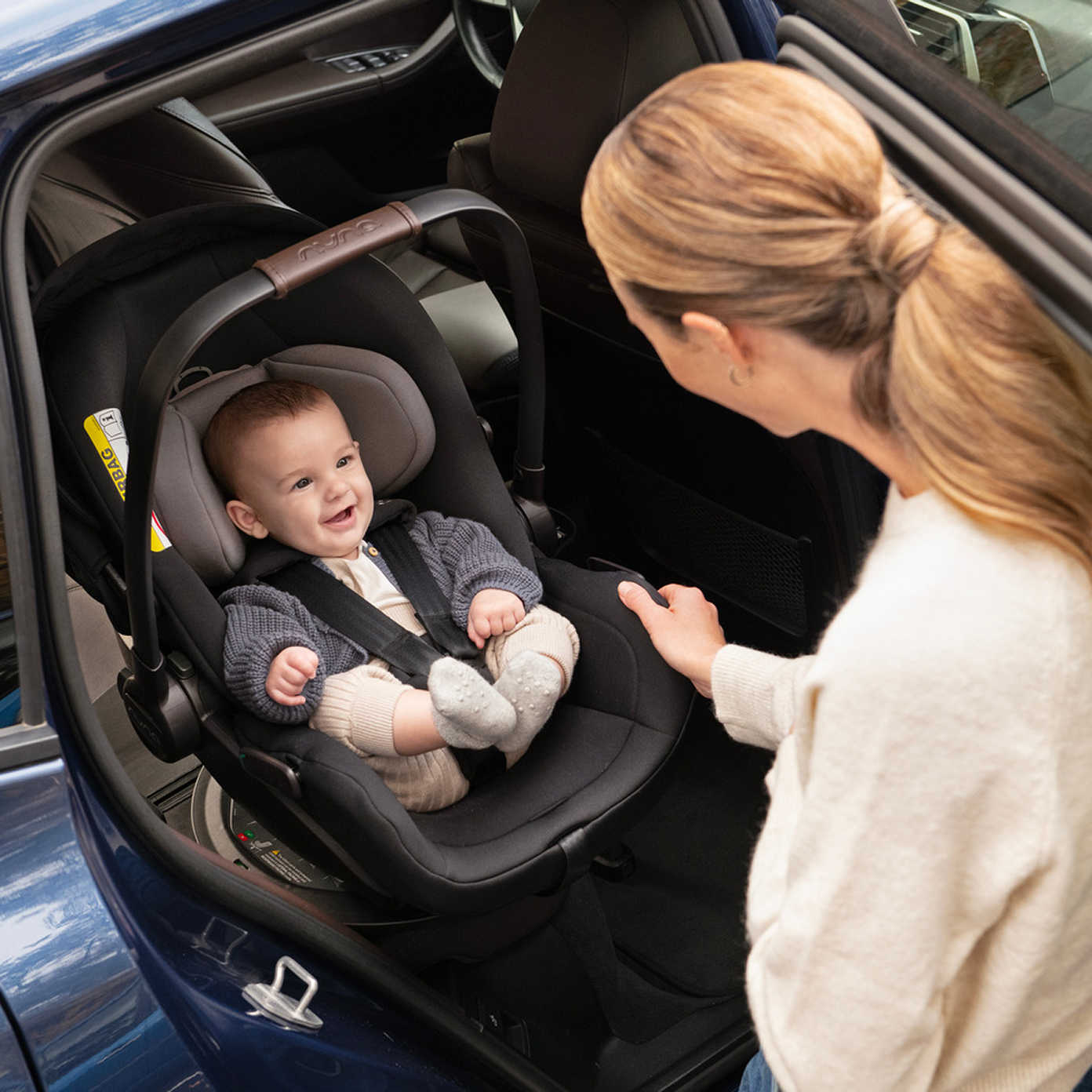 Smiling baby buckled into a Nuna infant car seat.