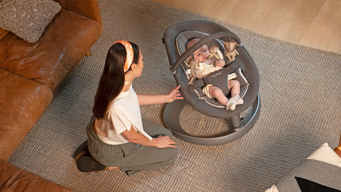 A mother sways her baby in the LEAF grow chair with detachable toy bar.